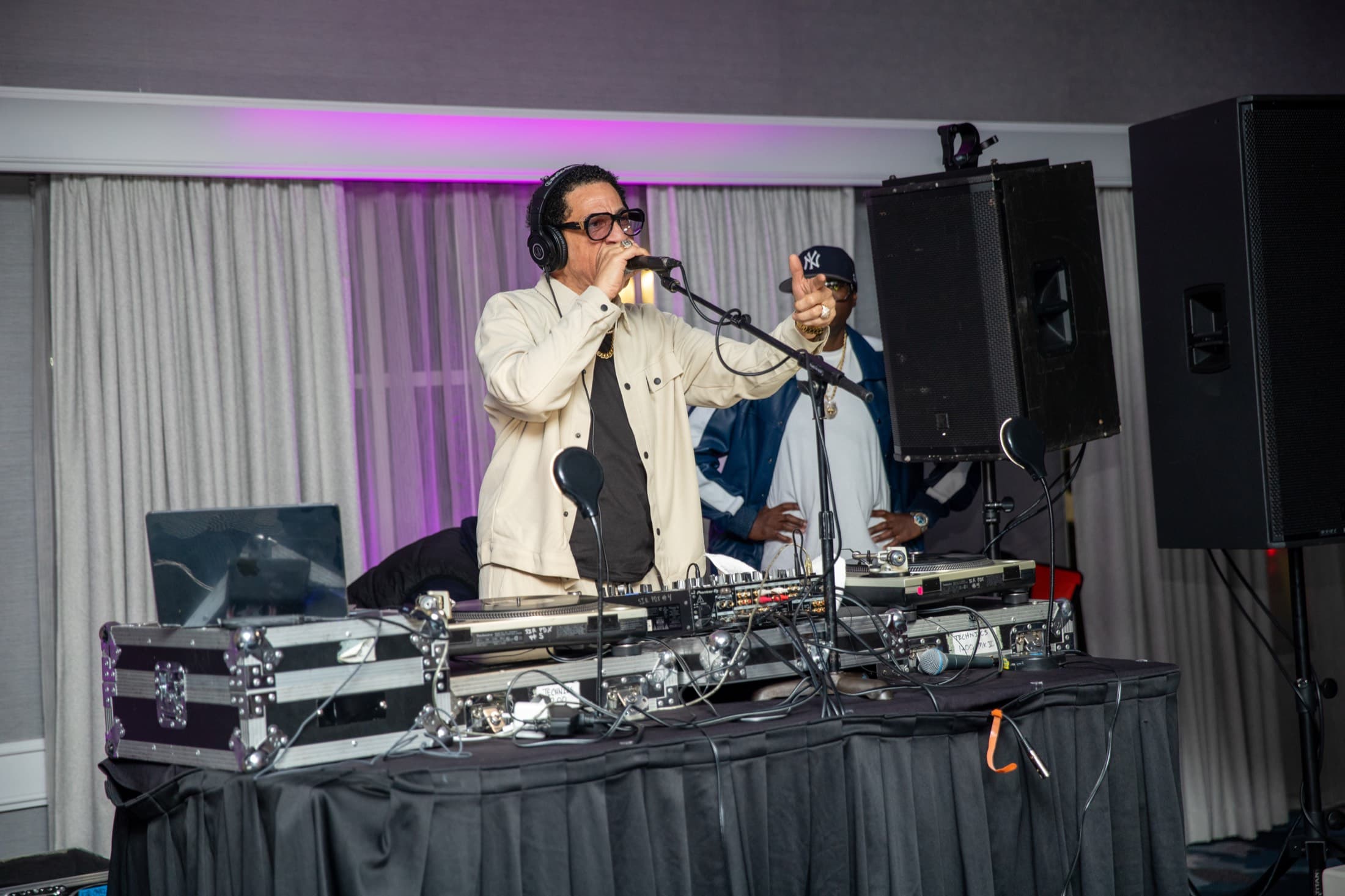 DJ performing at an event with turntables and microphone, purple accent lighting