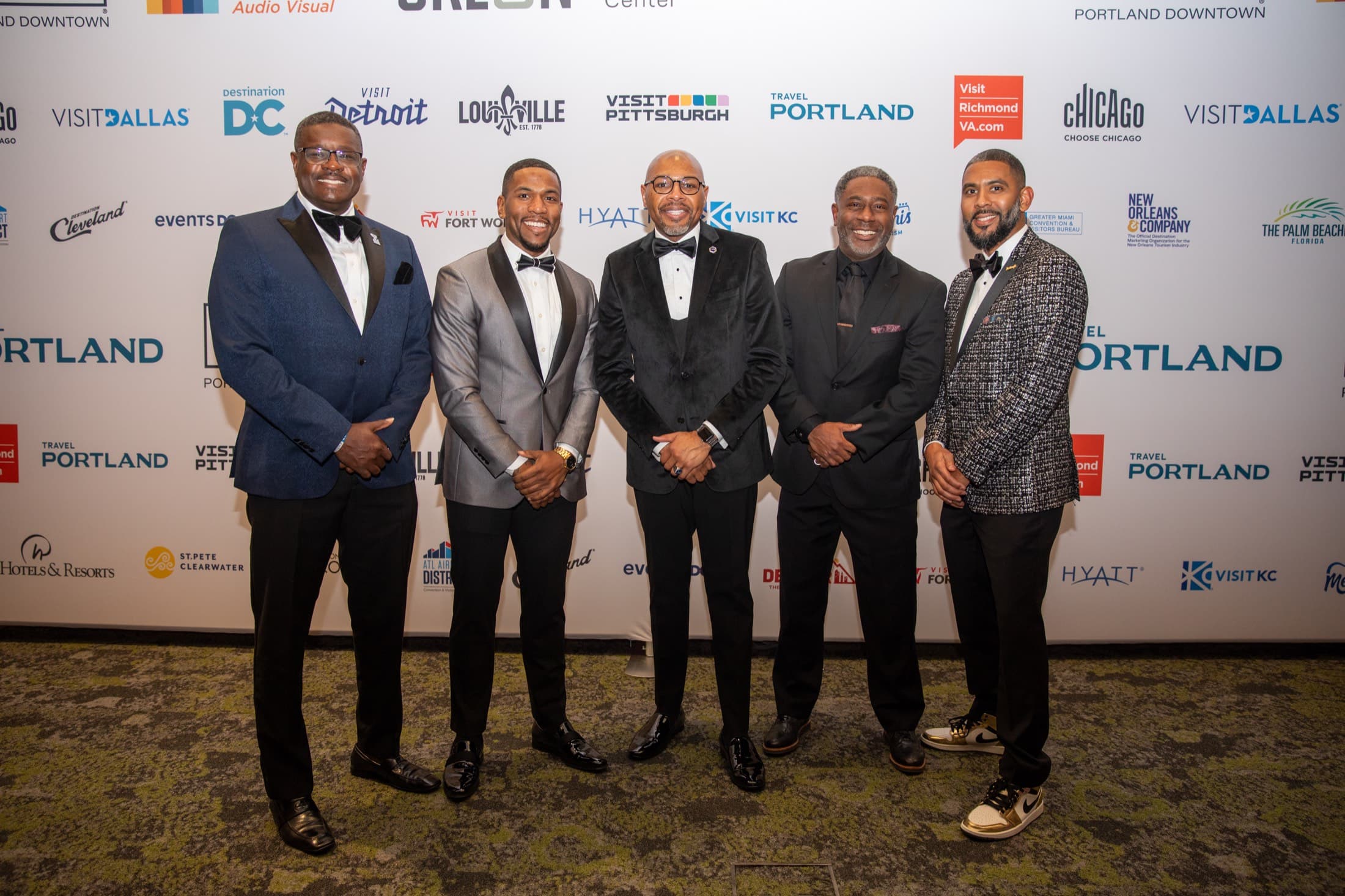 Group of guests in formal wear at an event, white sponsor backdrop